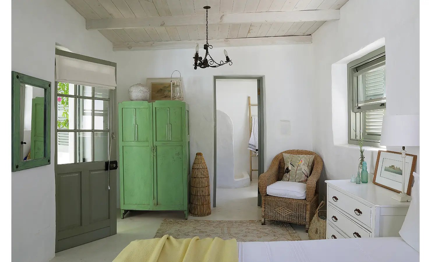 Perfect Hideaways: A light-filled bedroom with whitewashed walls, a green wardrobe, a wicker chair, and rustic decor elements. Farniente, Kommetjie.