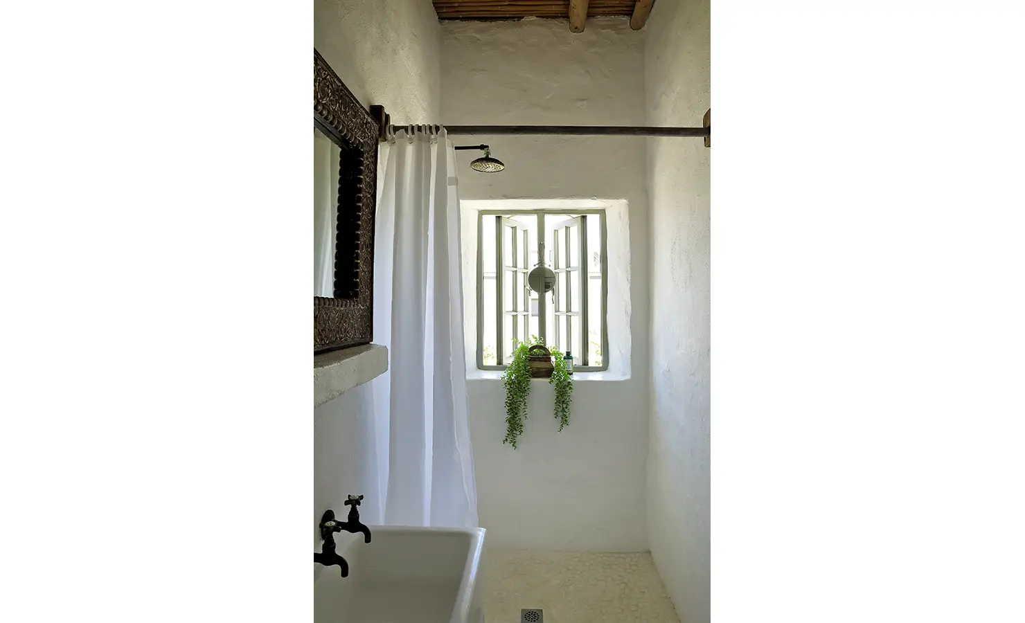 Perfect Hideaways: A small, light-filled shower room with a wooden-framed mirror, a potted plant on the windowsill, and an elegant white curtain. Farniente, Kommetjie.