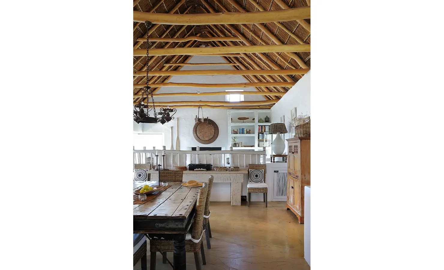 Perfect Hideaways: A cosy dining and living space with a wooden table, wicker chairs, and a thatched ceiling, exuding a warm coastal vibe. Farniente, Kommetjie.