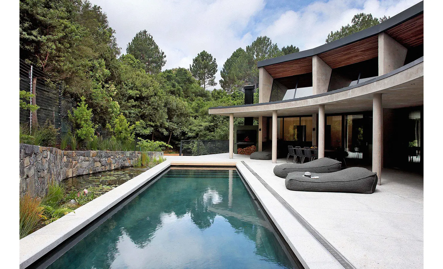 Perfect Hideaways: A minimalist pool terrace framed by forest, with stone walls, dark loungers, and a pristine swimming pool creating a calming outdoor haven. Villa Verte, Hout Bay.