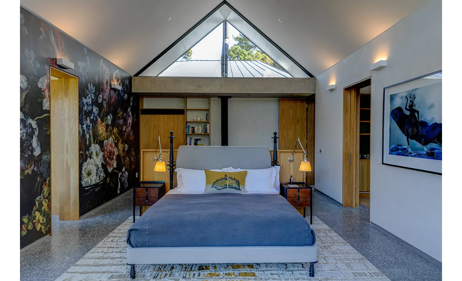 Perfect Hideaways: A serene bedroom with vaulted ceilings, dramatic floral mural, mid-century furniture, and a large triangular window bringing light and nature into the space. Villa Verte, Hout Bay.
