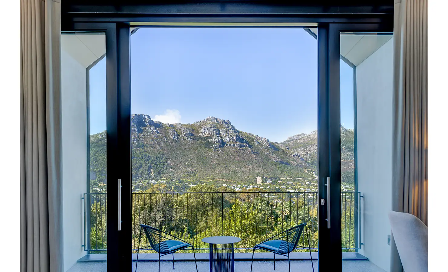Perfect Hideaways: A picture-perfect mountain view from a private balcony framed by large glass doors, with a small table and two chairs inviting relaxed moments in nature. Villa Verte, Hout Bay.