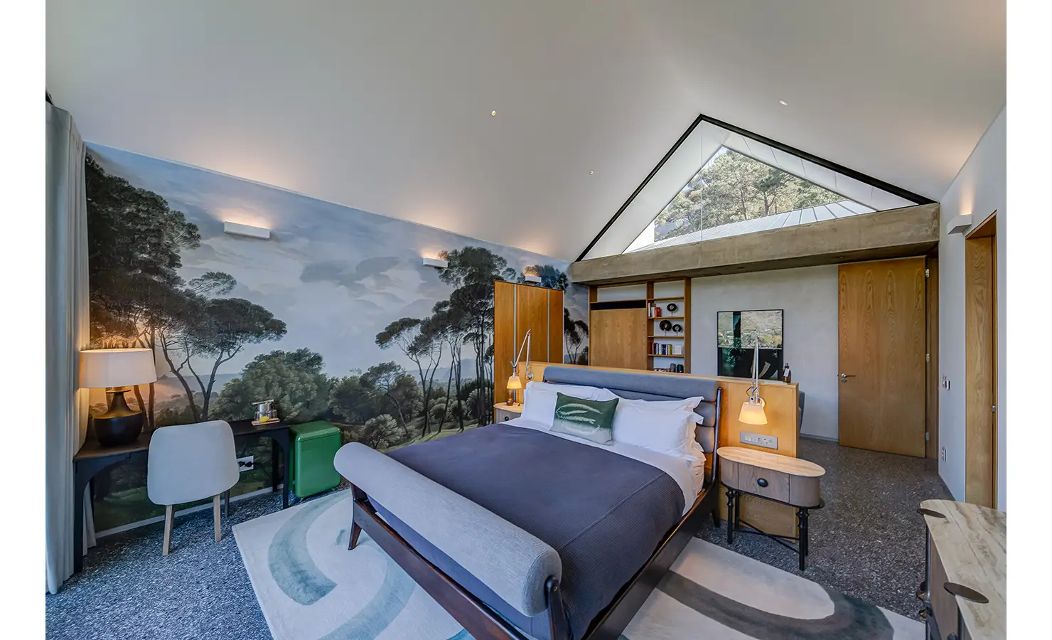 Perfect Hideaways: A dreamy bedroom with a forest mural, vaulted ceiling, warm wood accents, and a restful palette of blues and greens that echo the natural surroundings. Villa Verte, Hout Bay.