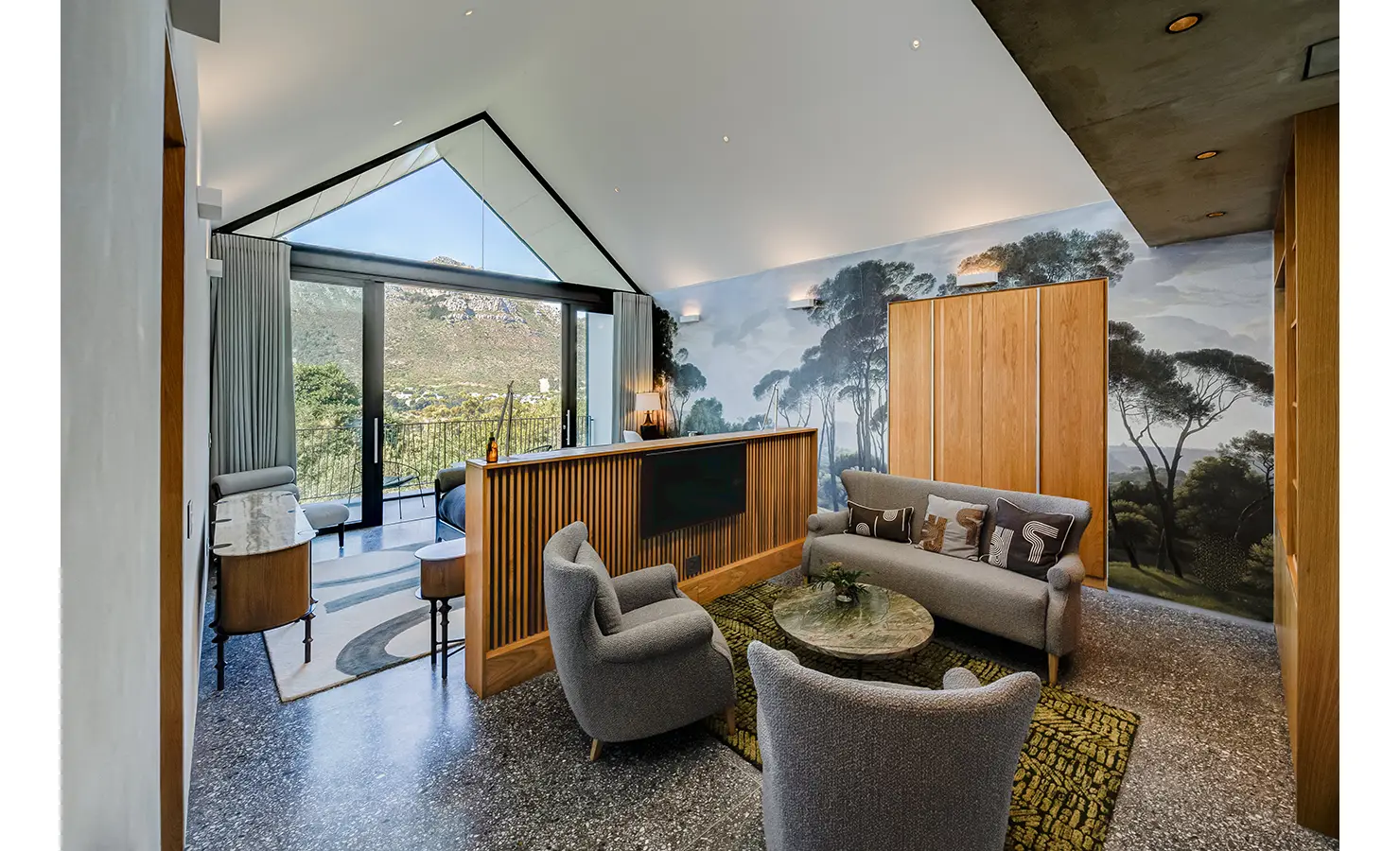 Perfect Hideaways: A sophisticated suite with a vaulted ceiling, muralled forest wall, soft grey seating and a balcony revealing breathtaking views of the Hout Bay valley. Villa Verte, Hout Bay.