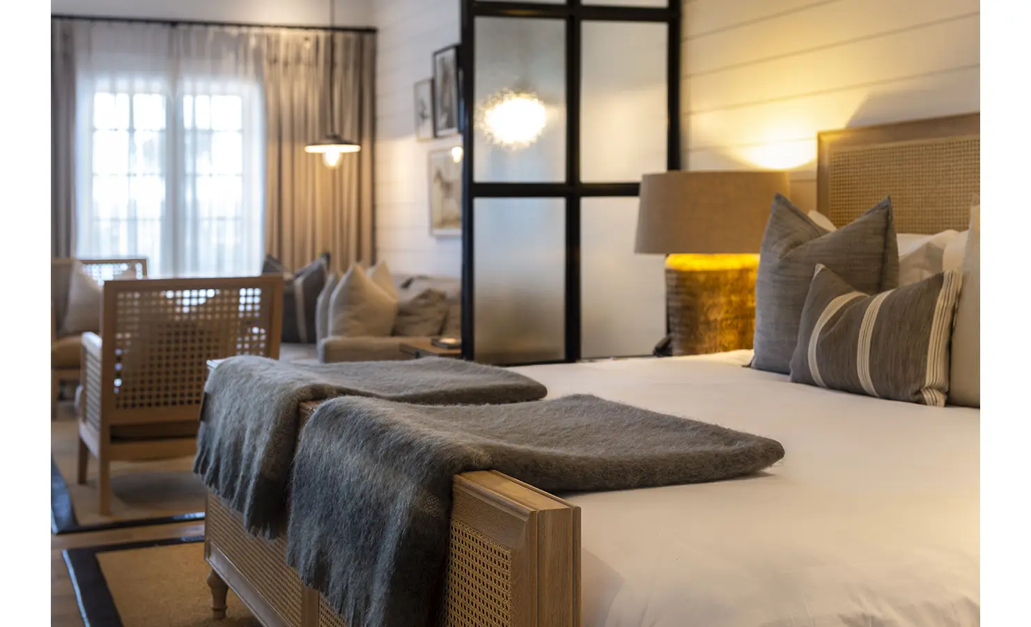 Perfect Hideaways: A luxurious bedroom featuring a large bed with grey throws, soft lighting, and a frosted glass partition. Riverdene, Shamwari Private Game Reserve.