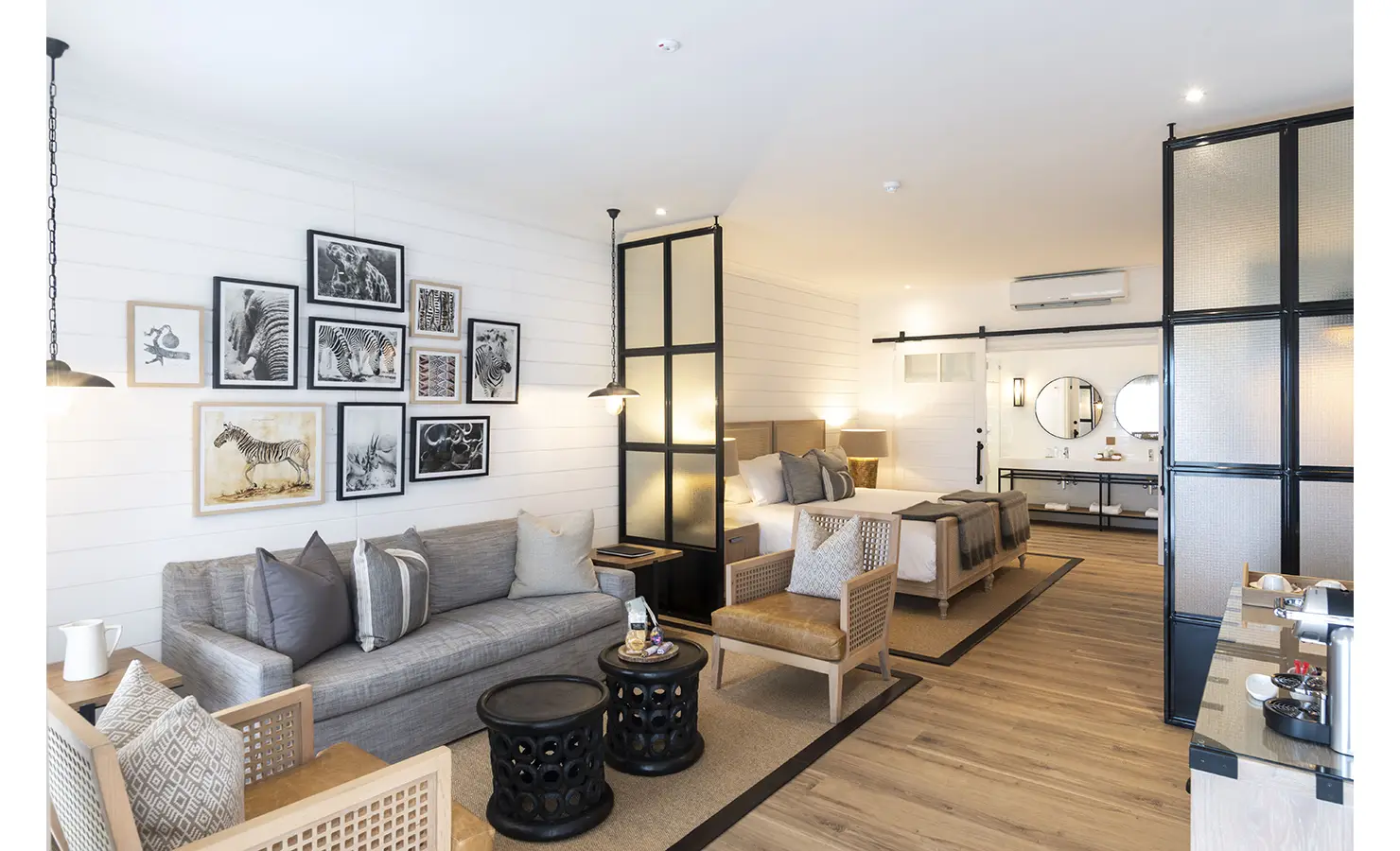 Perfect Hideaways: A spacious and stylish suite featuring a sitting area, a king-sized bed, animal-themed wall art, and a modern bathroom in the background. Riverdene, Shamwari Private Game Reserve.