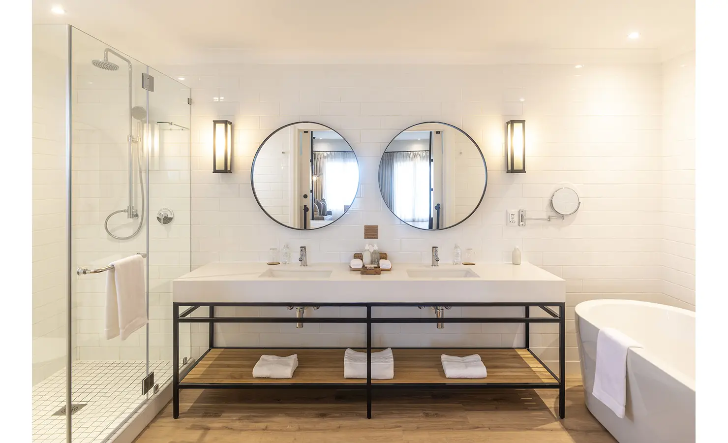 Perfect Hideaways: A contemporary bathroom with dual sinks, circular mirrors, a glass-enclosed shower, and a freestanding bathtub. Riverdene, Shamwari Private Game Reserve.