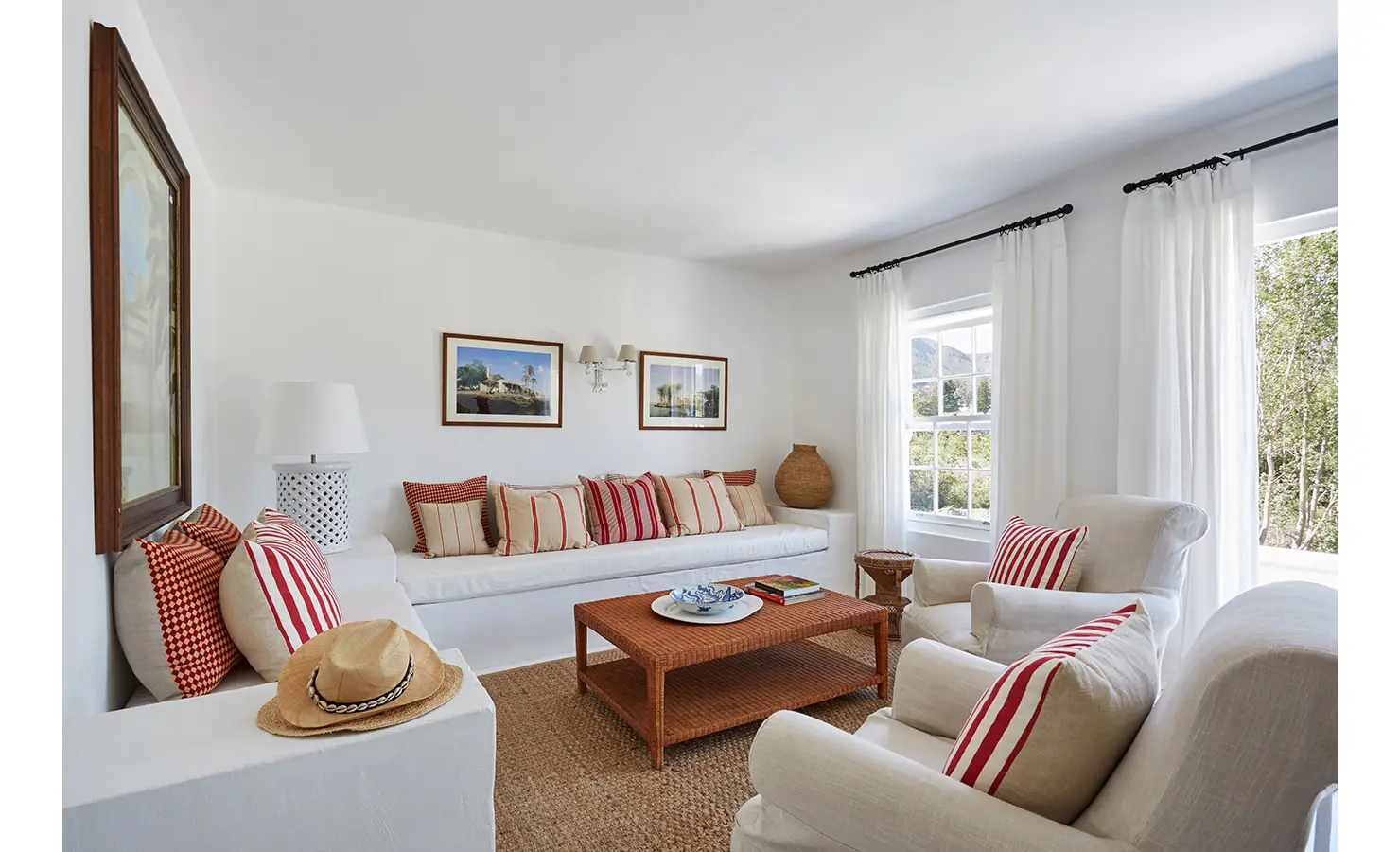 Perfect Hideaways: A bright and airy living room with a white built-in sofa adorned with red and cream striped cushions, armchairs, and large windows with flowing curtains. La Cotte Forest Cottages, Franschhoek.