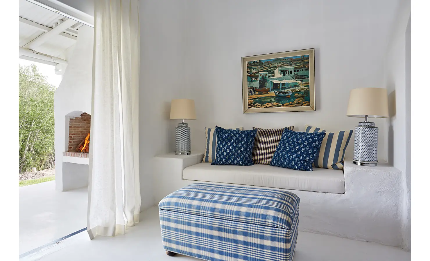 Perfect Hideaways: A cosy indoor nook with a built-in white bench, adorned with blue and patterned cushions, and a lit fireplace in the background. La Cotte Forest Cottages, Franschhoek.