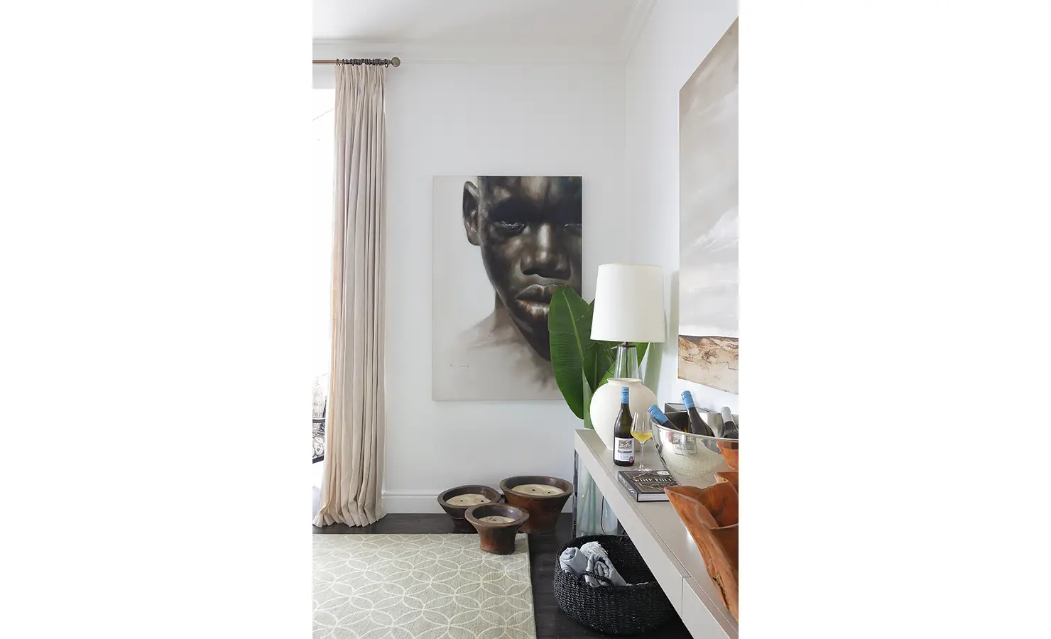 Perfect Hideaways: A striking portrait of a young boy with piercing eyes dominates this stylish corner, paired with earthy wooden stools and a sleek sideboard stocked with fine wine. A modern table lamp adds a soft glow to the space. Buitenzorg Estate, Constantia.