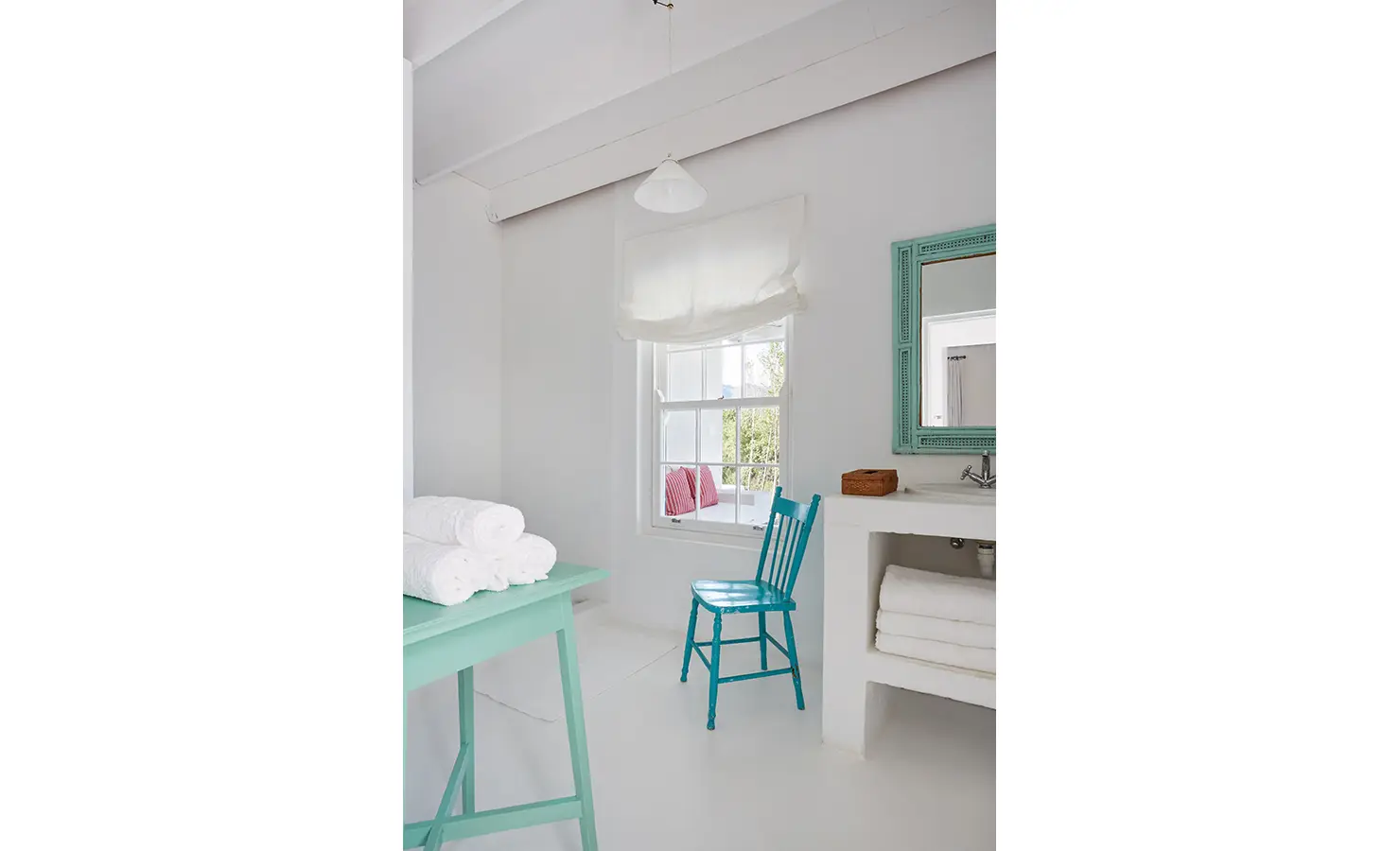Perfect Hideaways: A clean and minimalist bathroom with a turquoise chair, rolled white towels, and a window overlooking greenery. La Cotte Forest Cottages, Franschhoek.