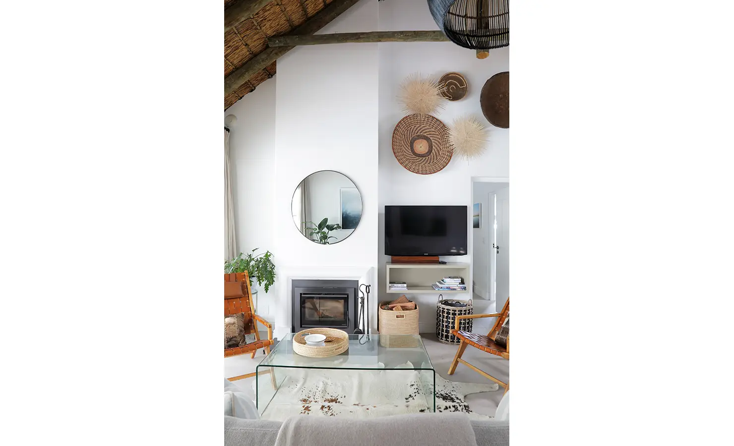 Perfect Hideaways: A cosy lounge area with a modern fireplace, round mirror, woven wall décor, and warm leather chairs, exuding a natural, rustic charm. Buitenzorg Estate, Constantia.