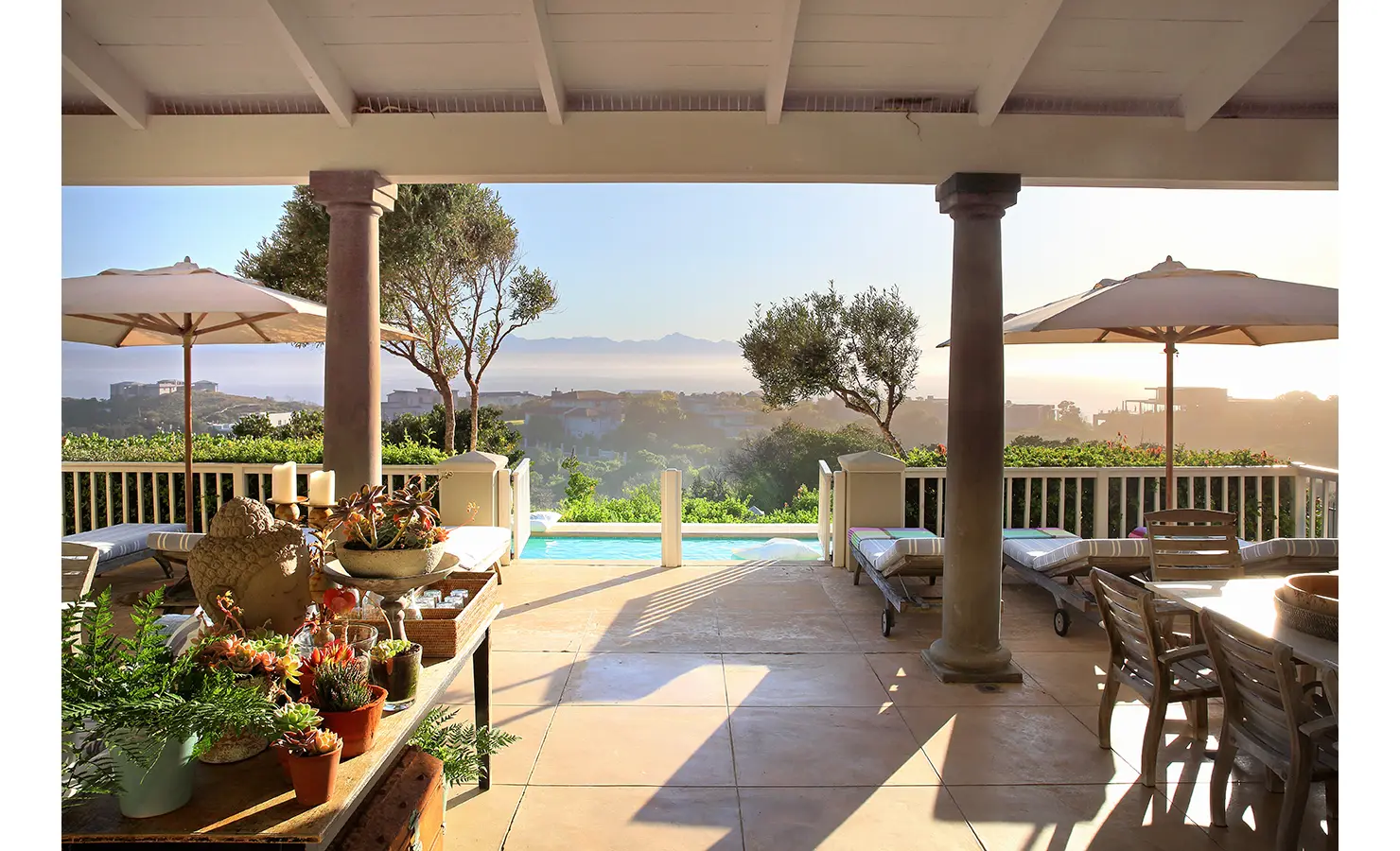 Perfect Hideaways: A stylish patio overlooking a pool and distant mountains, with comfortable outdoor seating, potted plants, and umbrellas creating a relaxing atmosphere. Beachwood On Robberg, Plettenberg Bay.