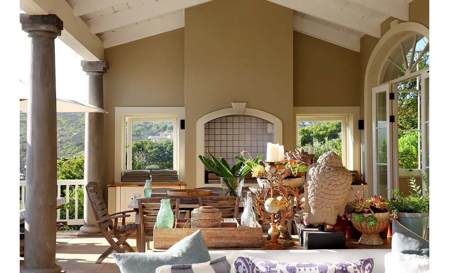 Perfect Hideaways: A cosy, semi-open outdoor lounge adorned with decorative elements, including a carved statue, woven baskets, and vibrant greenery, surrounded by serene natural views. Beachwood On Robberg, Plettenberg Bay.