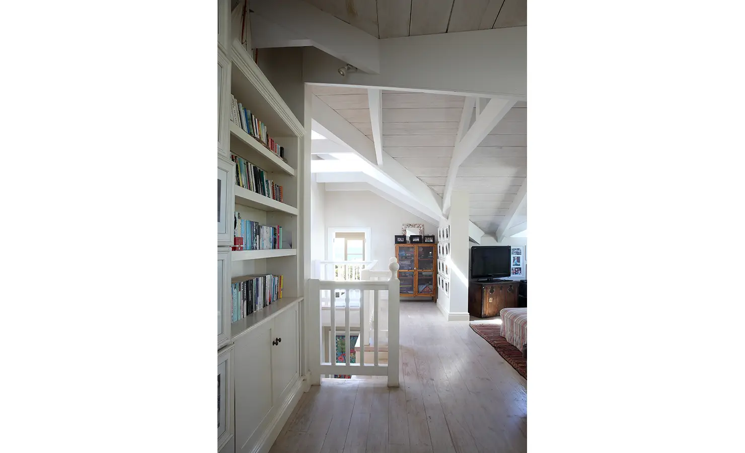 Perfect Hideaways: A charming loft space with built-in bookshelves, white-beamed ceilings, and cosy seating arrangements leading to a window with natural light. Beachwood On Robberg, Plettenberg Bay.