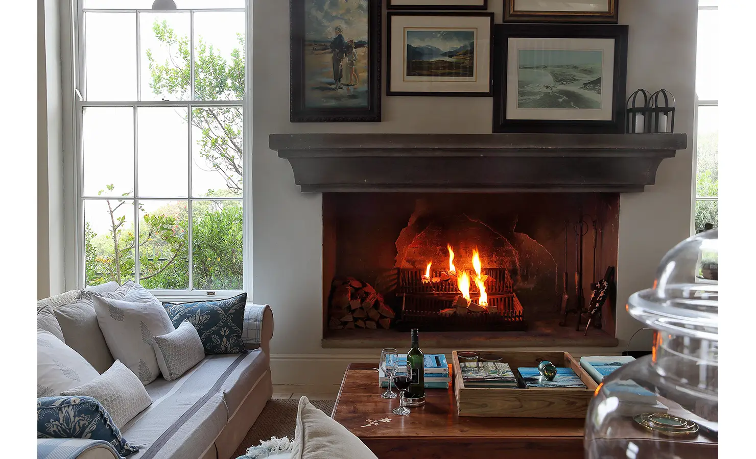 Perfect Hideaways: A cosy living room with a lit fireplace, framed artwork, and soft furnishings creating a warm and inviting atmosphere. Beachwood On Robberg, Plettenberg Bay.