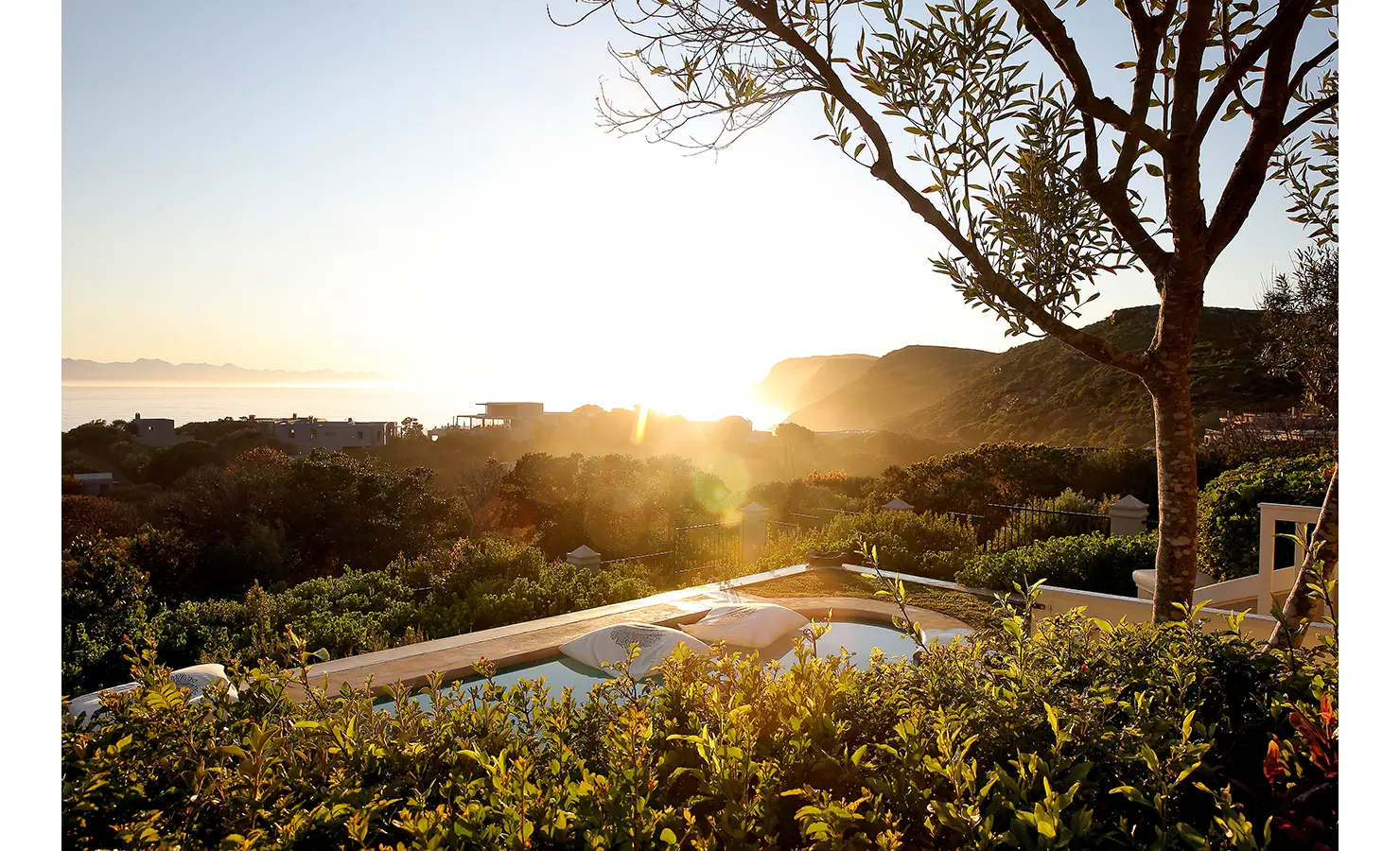 Perfect Hideaways: A scenic view of the garden and surrounding landscape, with distant cliffs and the ocean glowing in the golden hour light. Beachwood On Robberg, Plettenberg Bay.