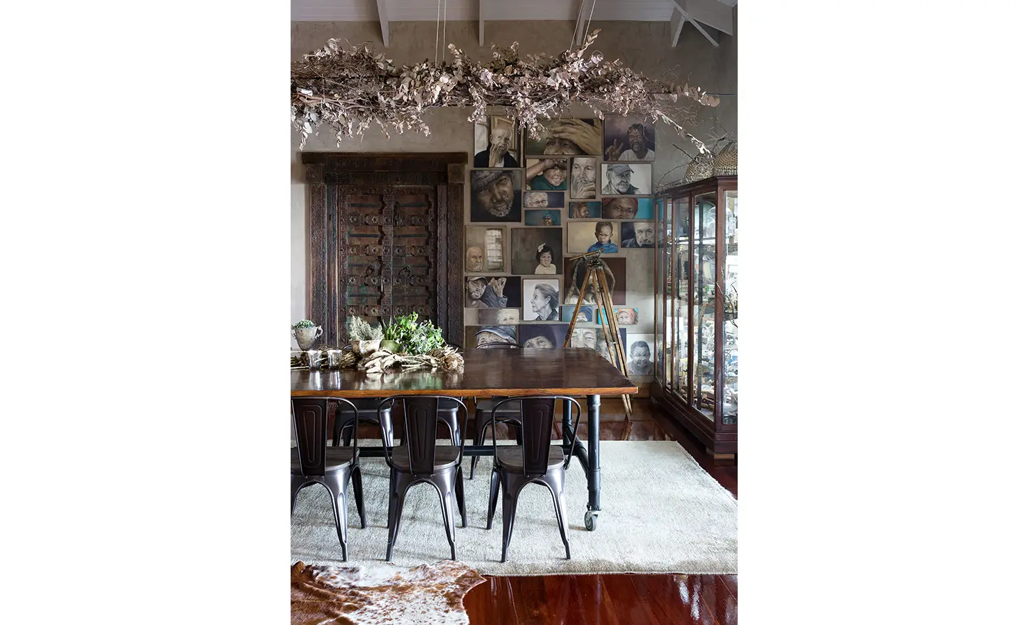 Perfect Hideaways: A captivating dining space featuring a rustic wooden table, industrial-style chairs, and an impressive gallery wall of expressive portraits. Above, dried foliage arrangements enhance the artistic atmosphere of this inviting setting. Sophias Retreat, Durban North.