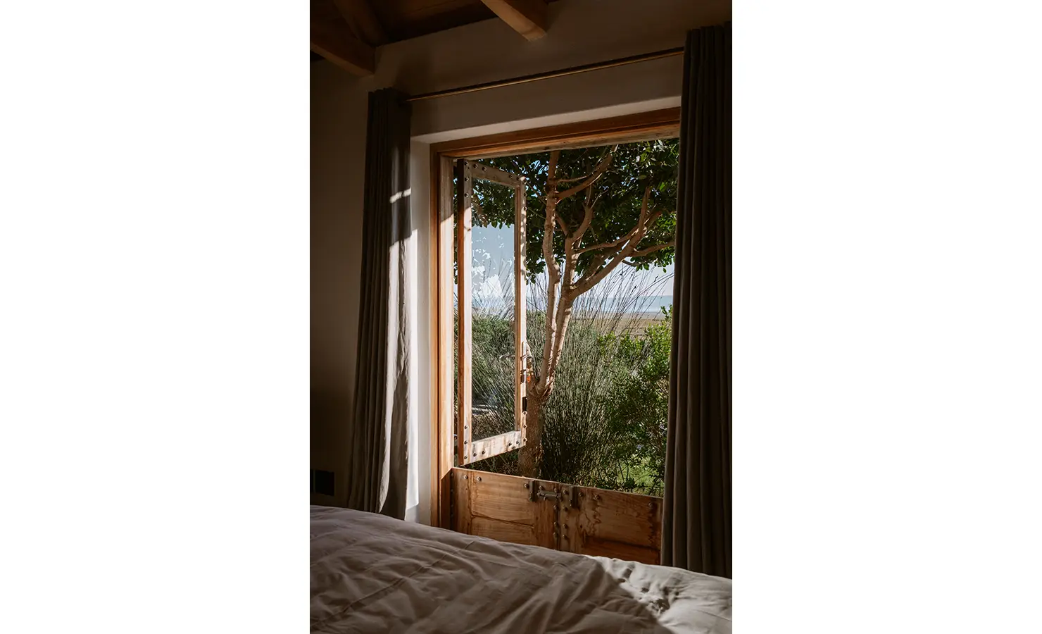Perfect Hideaways: Morning light streams through open stable-style bedroom doors, revealing a private view of tangled branches, reeds, and glimpses of the water beyond. Yellowwood Cottage, Churchhaven.