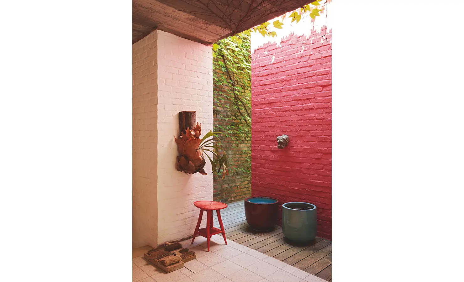 Perfect Hideaways: A small courtyard with vibrant red and white brick walls, decorative potted plants, and a rustic red stool under soft natural light. Johannesdal Manor, Stellenbosch.