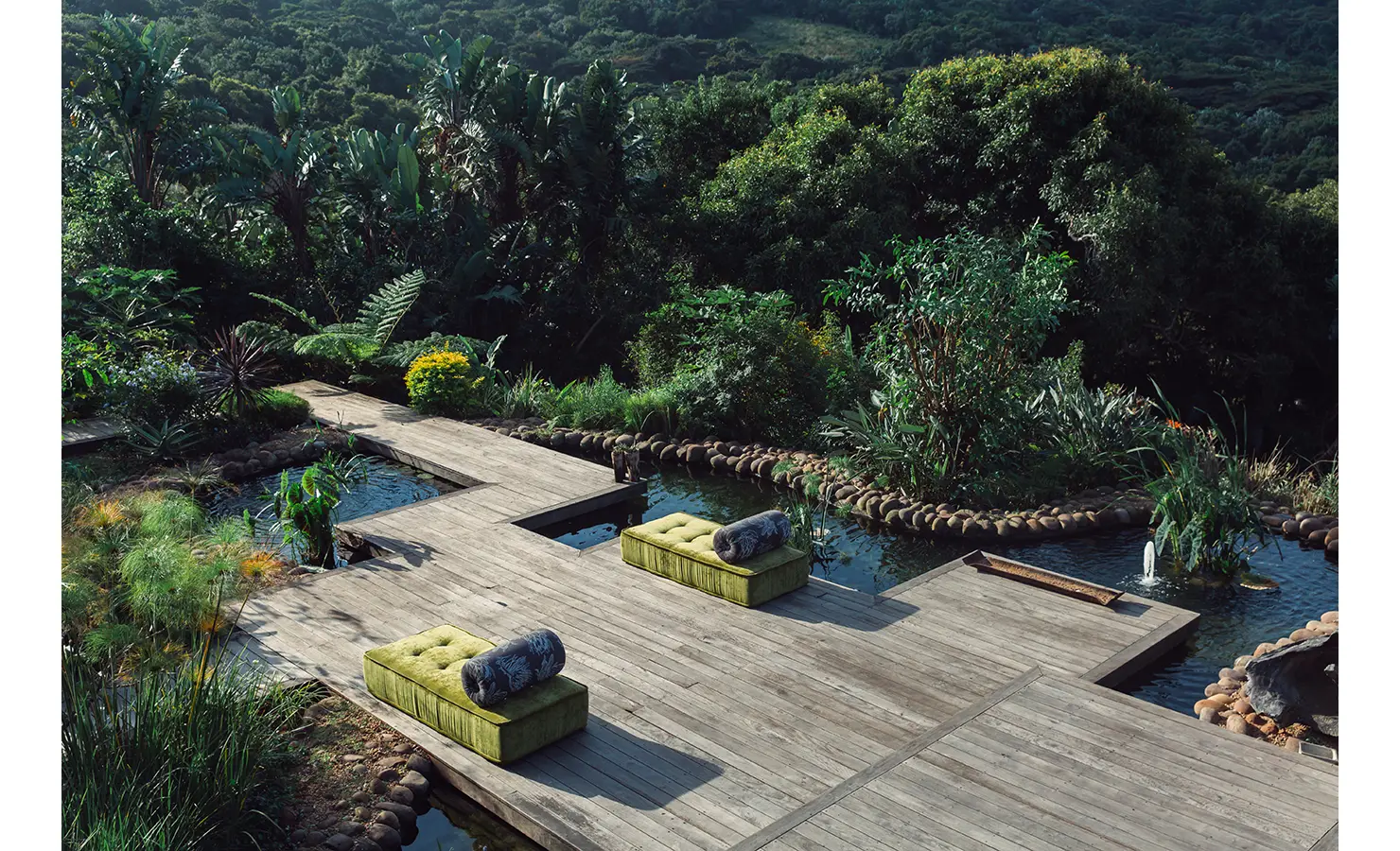 Perfect Hideaways: A stunning floating deck surrounded by lush greenery, overlooking a peaceful pond. Plush green ottomans provide a restful spot to take in the serene natural landscape. Sophias Retreat, Durban North.