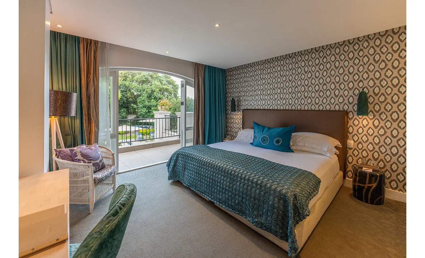 Perfect Hideaways: A serene bedroom opens onto a balcony, with botanical wallpaper, jewel-toned curtains, and a teal accent throw adding rich texture and colour. AtholPlace Hotel & Villa, Atholl.
