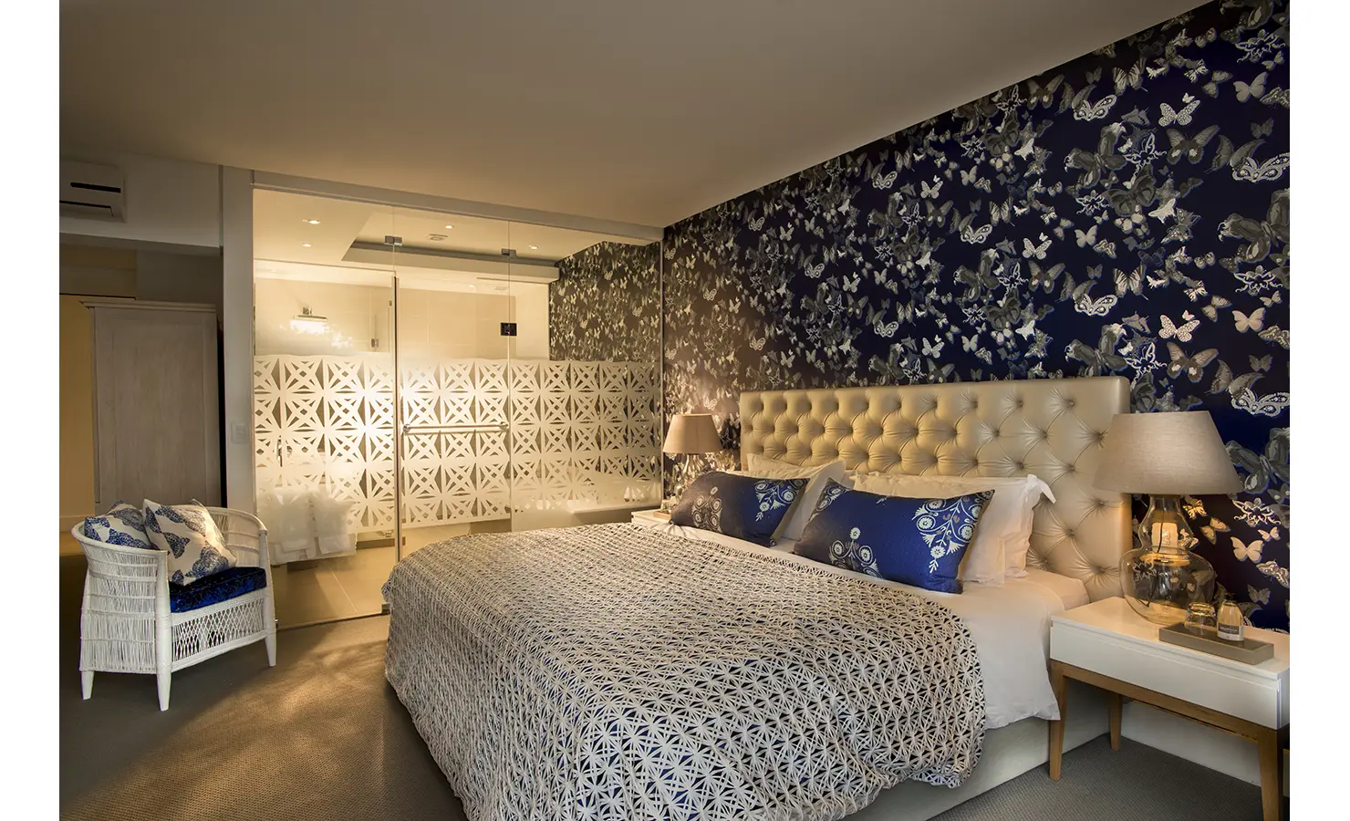 Perfect Hideaways: A luxurious bedroom with tufted headboard and butterfly wallpaper exudes glamour, with elegant bedside lamps and plush bedding in blue and cream. AtholPlace Hotel & Villa, Atholl.
