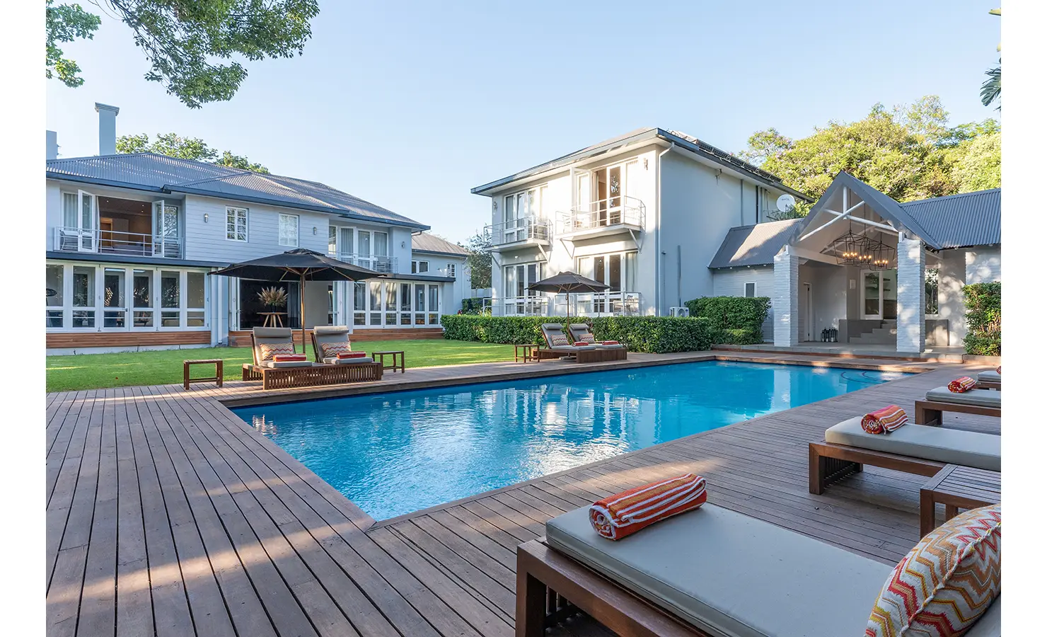 Perfect Hideaways: A spacious pool deck connects two elegant villa wings, with wooden loungers and monochrome umbrellas adding a refined resort feel. AtholPlace Hotel & Villa, Atholl.