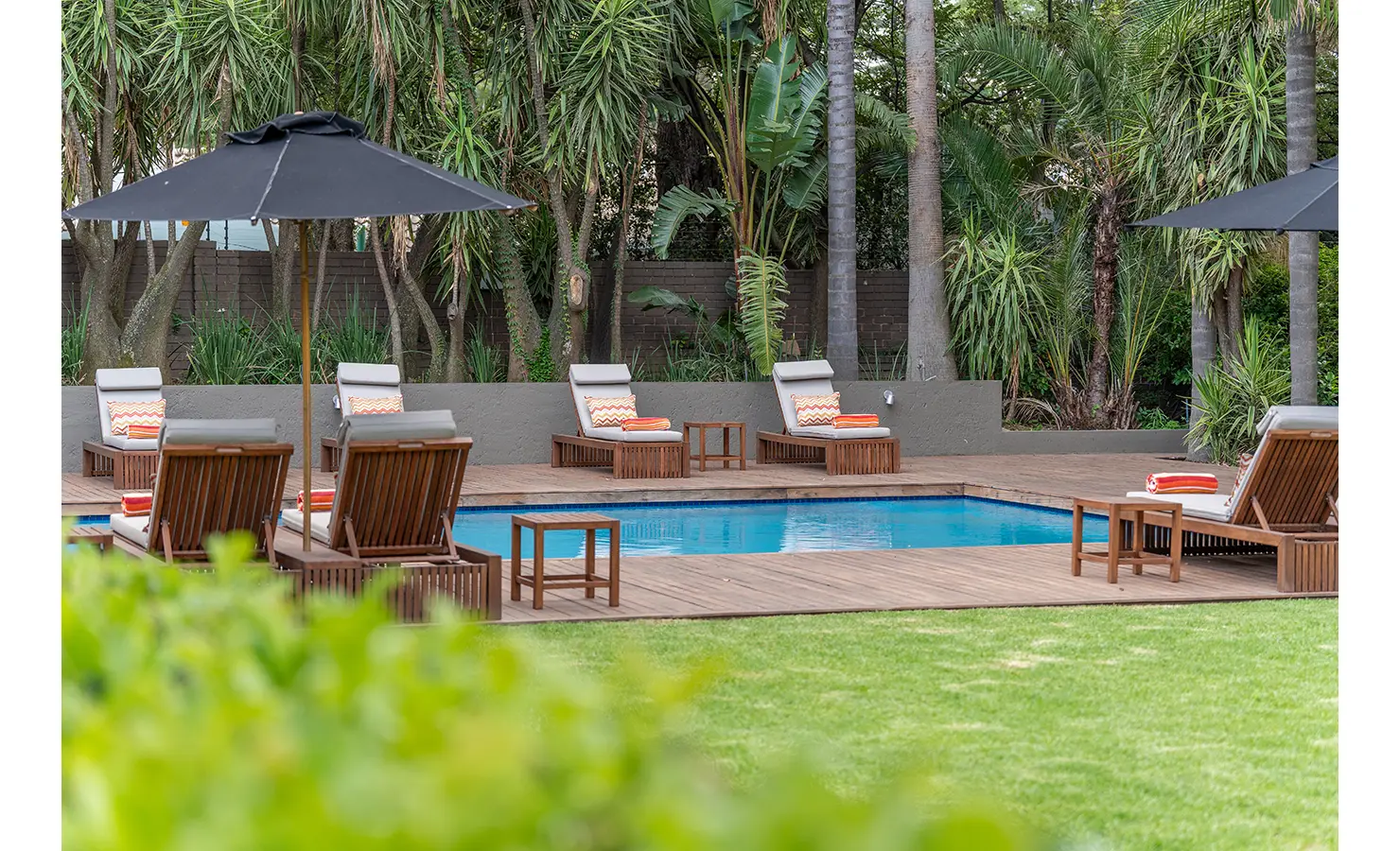 Perfect Hideaways: A tropical garden encloses a second serene pool area with wooden loungers, orange-striped towels, and black parasols, perfect for relaxed afternoons. AtholPlace Hotel & Villa, Atholl.