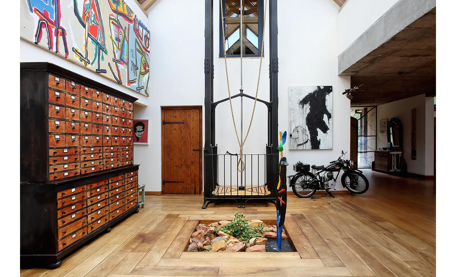 Perfect Hideaways. A spacious, art-filled room with wooden flooring features a tall metal structure. There's a large cabinet with many drawers, colorful artwork on the walls, and a motorcycle parked in the corner. Gaia, Constantia.