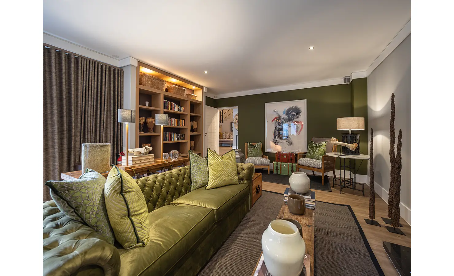 Perfect Hideaways: An elegant library lounge features a deep olive velvet sofa, curated bookshelves, and eclectic art pieces, inviting quiet moments of reflection. AtholPlace Hotel & Villa, Atholl.