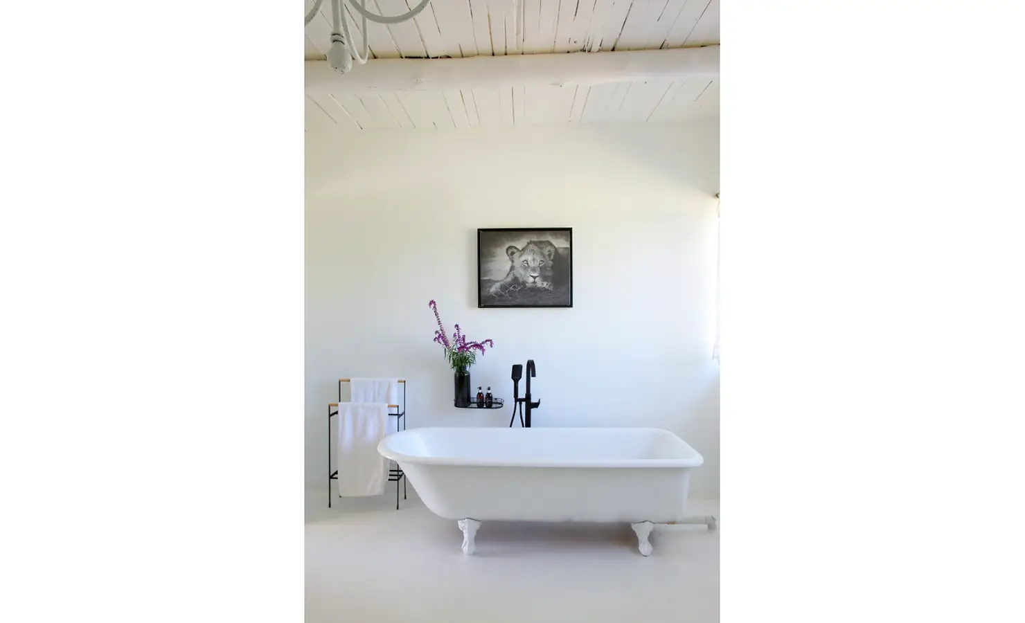 Perfect Hideaways: A vintage-style bathroom featuring a freestanding clawfoot tub, floral decor, and a black-and-white lion cub portrait on the wall. Owlswood, Buffelspoort.