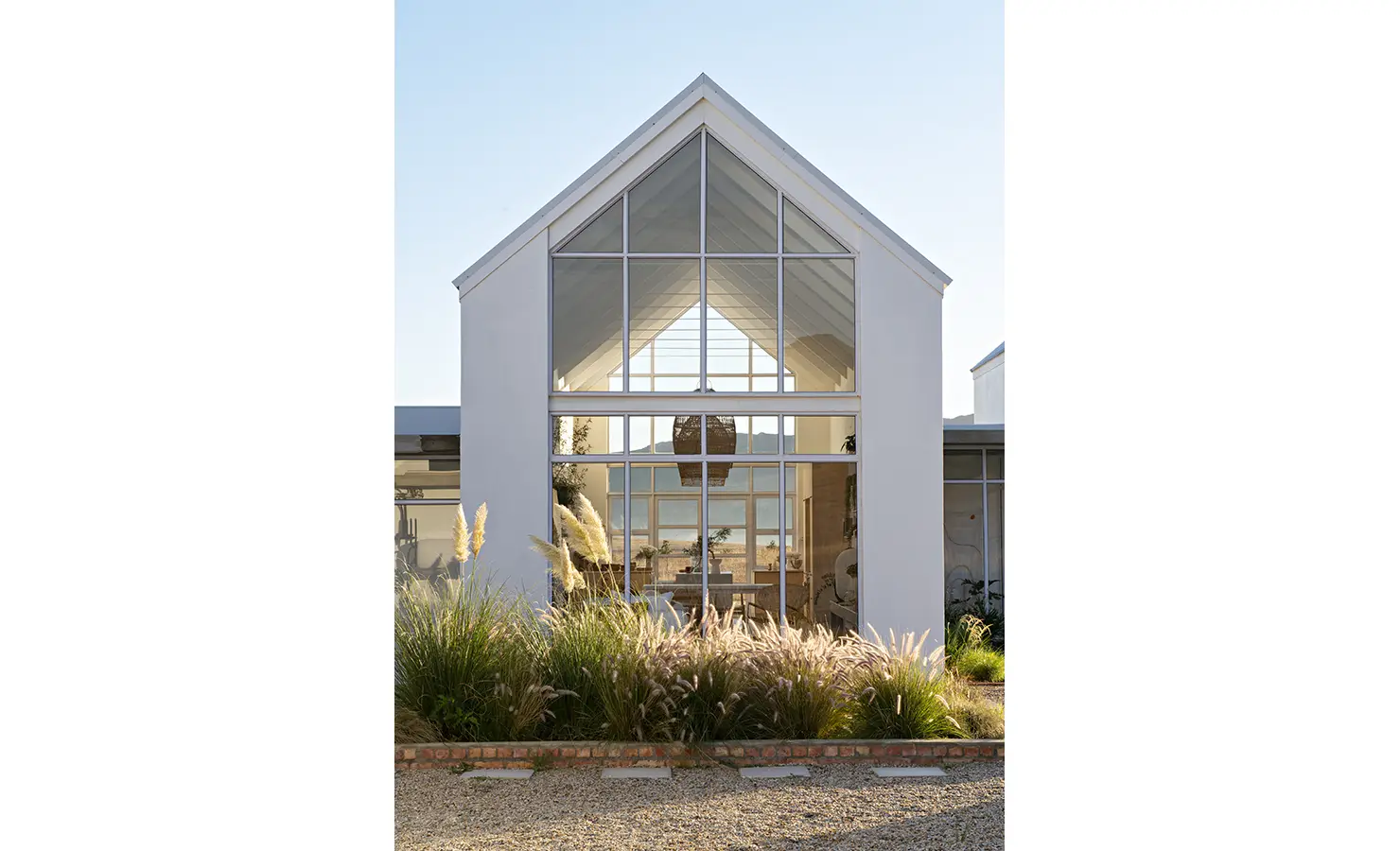 Perfect Hideaways: Symmetrical gabled façade with expansive glass panels framed by ornamental grasses, offering views through to the mountains beyond, Thuúla Haven, Hemel-en-Aarde.