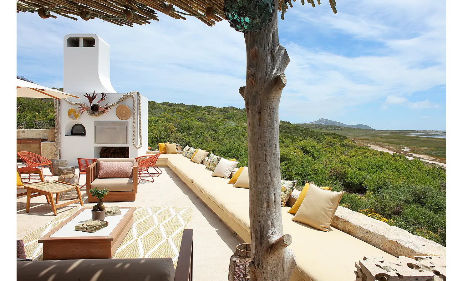 Perfect Hideaways: A beautifully designed outdoor terrace with a built-in braai and pizza oven, decorated with nautical elements, woven lanterns, and a long cushioned bench that offers breathtaking views of the lush green landscape and distant lagoon. Flamingo, Churchhaven.