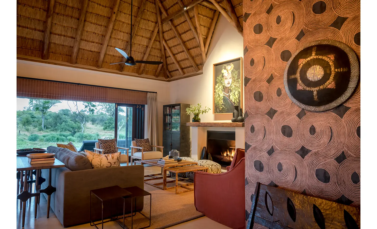 Perfect Hideaways: A stylish living area with a feature wall adorned with geometric patterns, a fireplace, and large glass doors offering a view of the surrounding nature. Tulela Lodge, Klaserie Private Nature Reserve.
