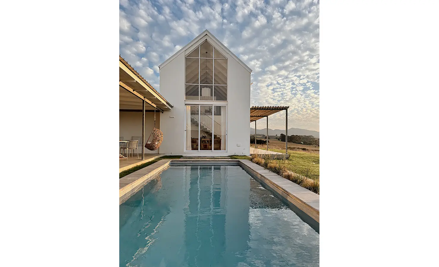 Perfect Hideaways: Narrow lap pool framed by a gabled façade and pergola-covered seating areas, set against open countryside, Thuúla Haven, Hemel-en-Aarde.