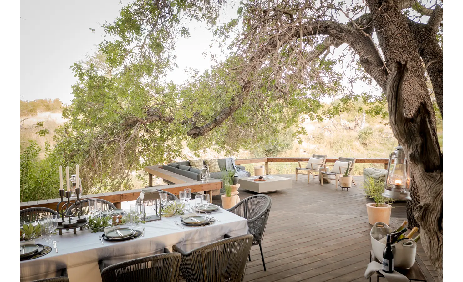 Perfect Hideaways: An inviting outdoor deck with a long dining table set under a tree canopy, overlooking a tranquil bush landscape. Tulela Lodge, Klaserie Private Nature Reserve.