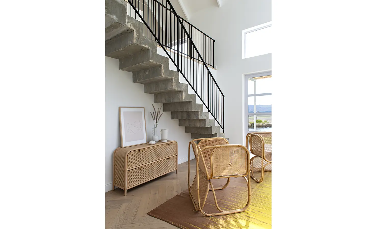 Perfect Hideaways: Minimalist staircase with raw concrete treads and black railing, complemented by rattan chairs and console table, Thuúla Haven, Hemel-en-Aarde.