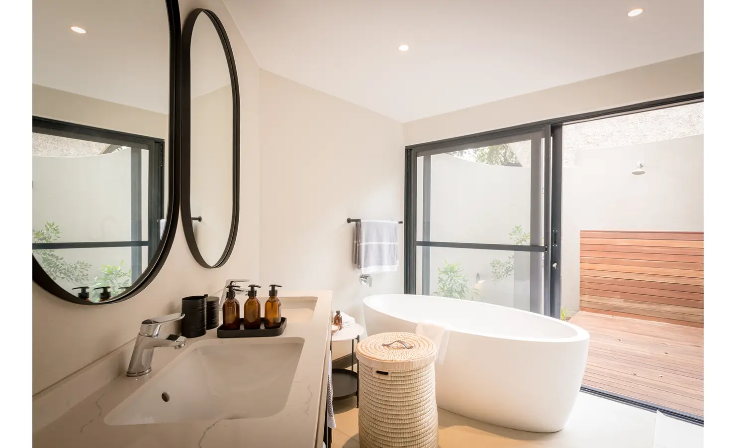 Perfect Hideaways: A modern bathroom with a sleek freestanding bathtub, large mirrors, and a view of an enclosed outdoor shower area. Tulela Lodge, Klaserie Private Nature Reserve.