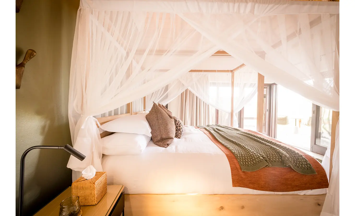 Perfect Hideaways: A cosy bedroom with soft natural lighting, a four-poster bed draped with a white canopy, and warm, earthy tones. Tulela Lodge, Klaserie Private Nature Reserve.