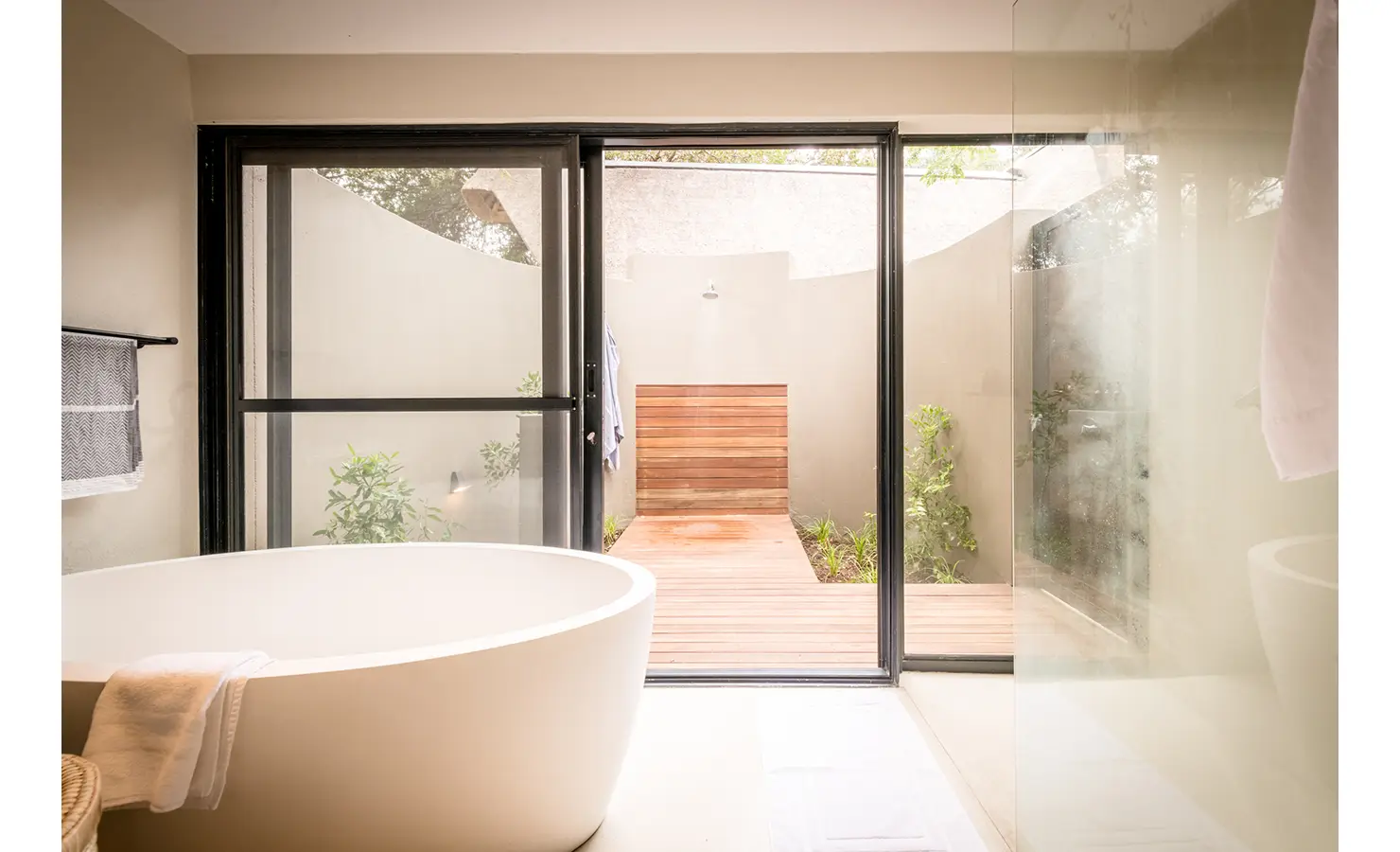 Perfect Hideaways: A contemporary bathroom with a freestanding bathtub, glass doors opening to a private outdoor shower area, and minimalist design elements. Tulela Lodge, Klaserie Private Nature Reserve.