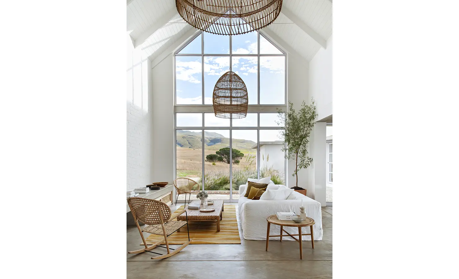 Perfect Hideaways: Bright double-volume lounge with wicker accents, white sofa, and floor-to-ceiling windows framing rolling countryside views, Thuúla Haven, Hemel-en-Aarde.