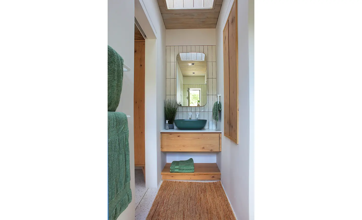 Perfect Hideaways: A compact yet stylish bathroom with a green ceramic basin, a wood-finished floating vanity, and a large mirror reflecting soft natural light, accented with earthy textures and greenery. Flamingo, Churchhaven.