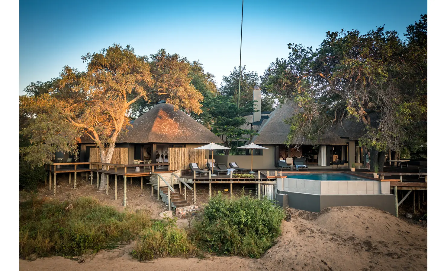 Perfect Hideaways: A view of the lodge with its thatched roofs and expansive wooden deck, complete with a pool and sun loungers, blending seamlessly into the natural surroundings. Tulela Lodge, Klaserie Private Nature Reserve.