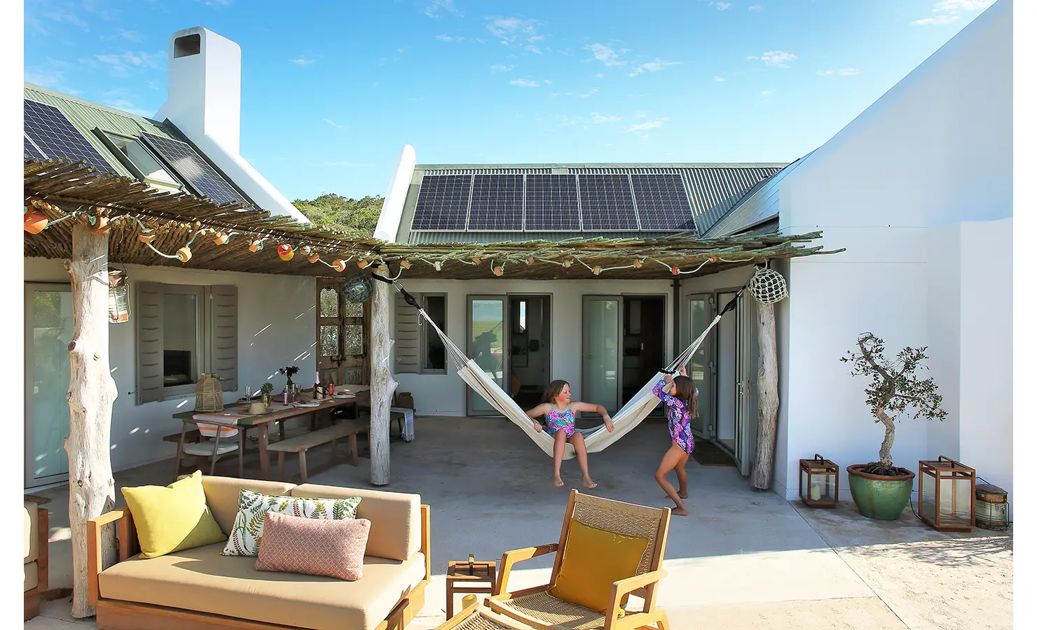 Perfect Hideaways: A sun-drenched courtyard featuring an ancient olive tree, a stone bench with plush cushions, and high textured walls offering a peaceful, private escape. Flamingo, Churchhaven.