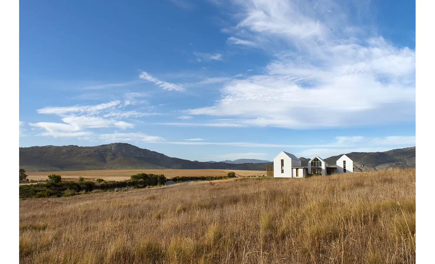 Perfect Hideaways: Remote modern farmhouse with gabled roofs set in expansive golden grasslands under a vast blue sky, Thuúla Haven, Hemel-en-Aarde.