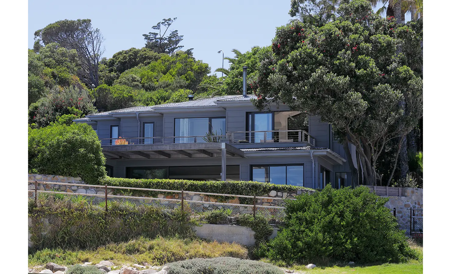 Perfect Hideaways: A striking beachfront home nestled among lush foliage, with expansive glass windows and a spacious terrace offering breathtaking ocean views. Oasis On Glen, Camps Bay.