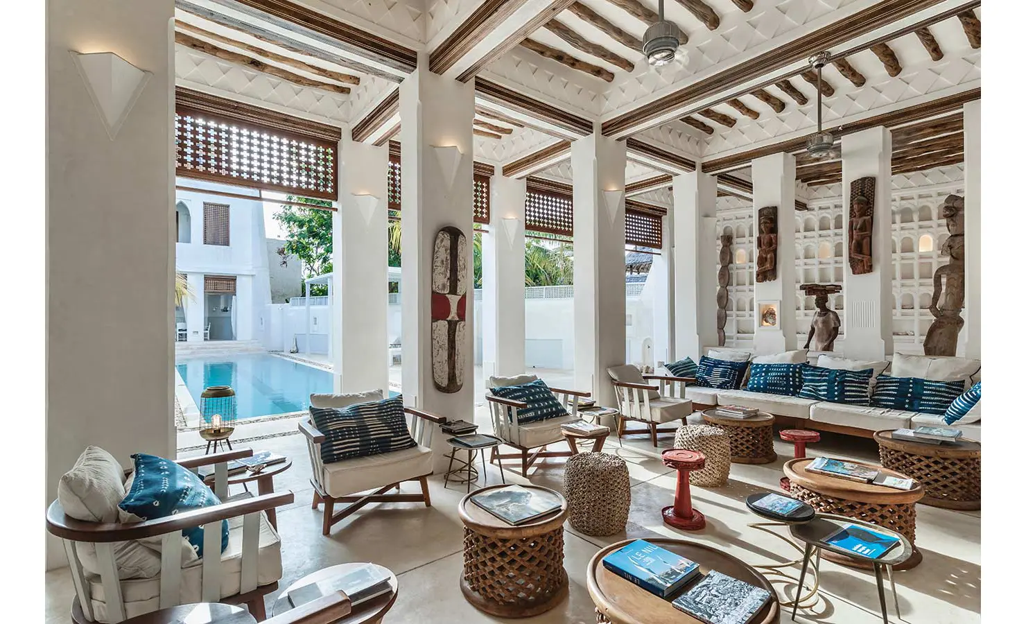 Perfect Hideaways: A spacious and open sitting area with white walls, wooden ceiling beams, eclectic furniture, and decor, offering views of a serene outdoor pool. The Kasbah, Lamu.