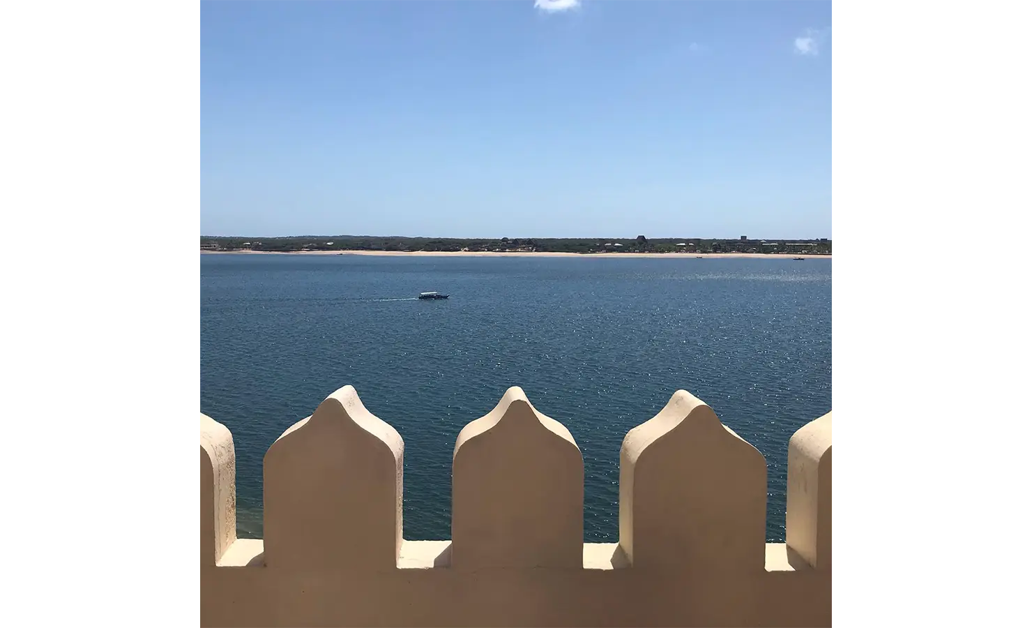 Perfect Hideaways: A picturesque ocean view framed by Swahili-inspired decorative railings, with a boat gliding across the water. Shela Beach House, Lamu.