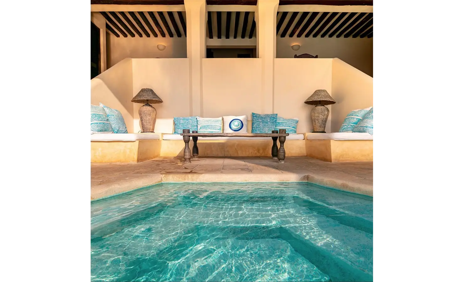 Perfect Hideaways: A refreshing pool surrounded by cosy seating adorned with vibrant cushions, blending traditional and modern decor. Shela Beach House, Lamu.
